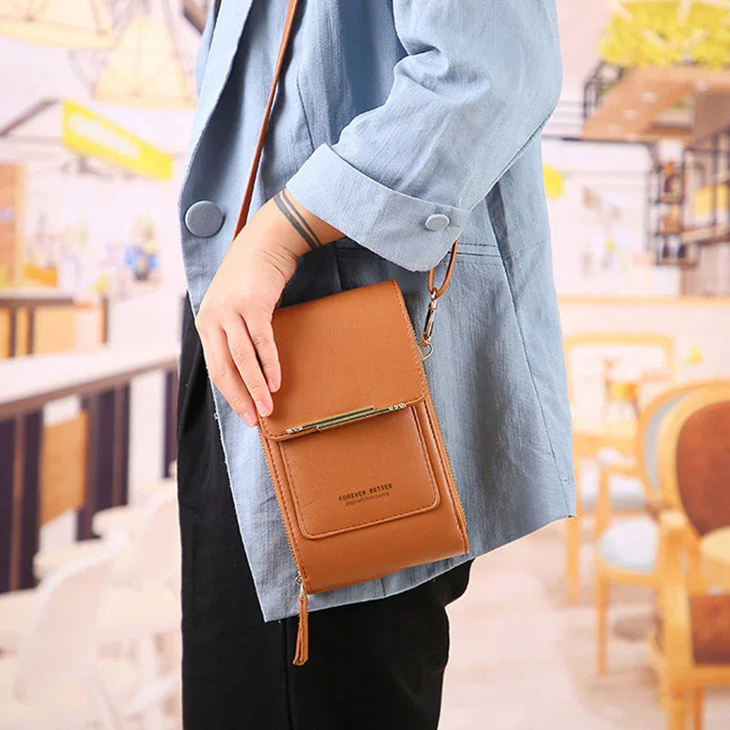 Person in blue jacket holding tan leather crossbody wallet bag with front pocket in cafe