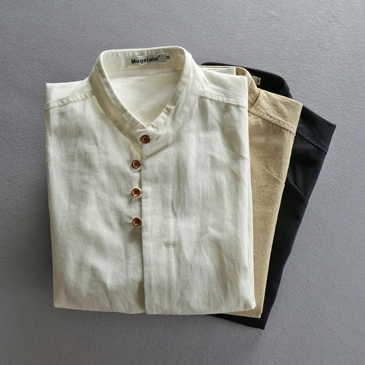 Folded casual shirts in white, beige, and black with wooden buttons on gray background