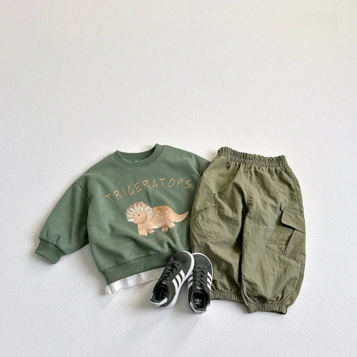 Kids outfit with green Triceratops sweatshirt, olive cargo pants, and black Adidas sneakers on white