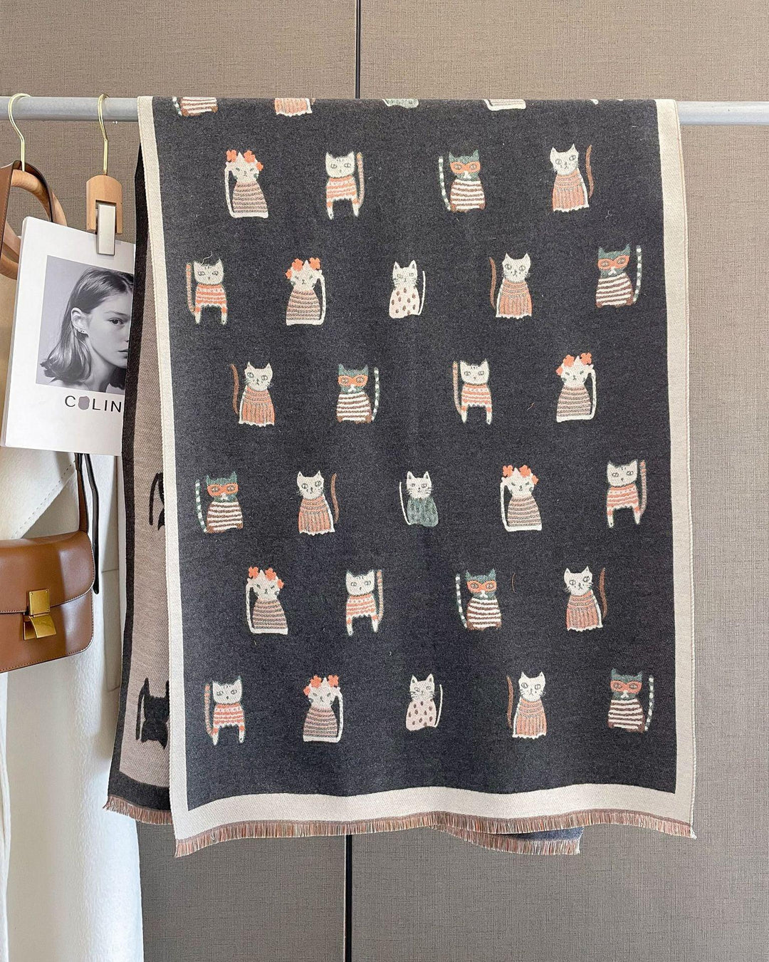 Dark gray wool scarf with cute cat and flower pattern hanging on a rack beside brown handbag