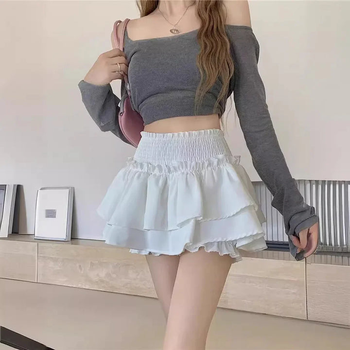 Woman wearing gray off-shoulder crop top and white layered ruffle mini skirt indoors