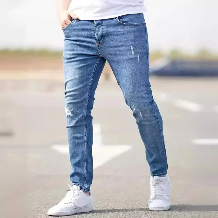 Person wearing slim fit distressed blue jeans and white sneakers standing outdoors on pavement