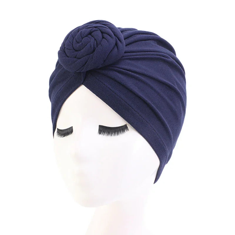 Navy blue turban headwrap with rose knot detail on white mannequin with long eyelashes