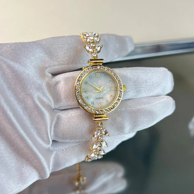 Elegant gold quartz wristwatch with crystal-studded bezel and leaf-pattern bracelet held in white glove