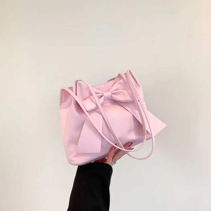 Hand holding a pastel pink tote bag with long straps and a decorative bow against a plain background