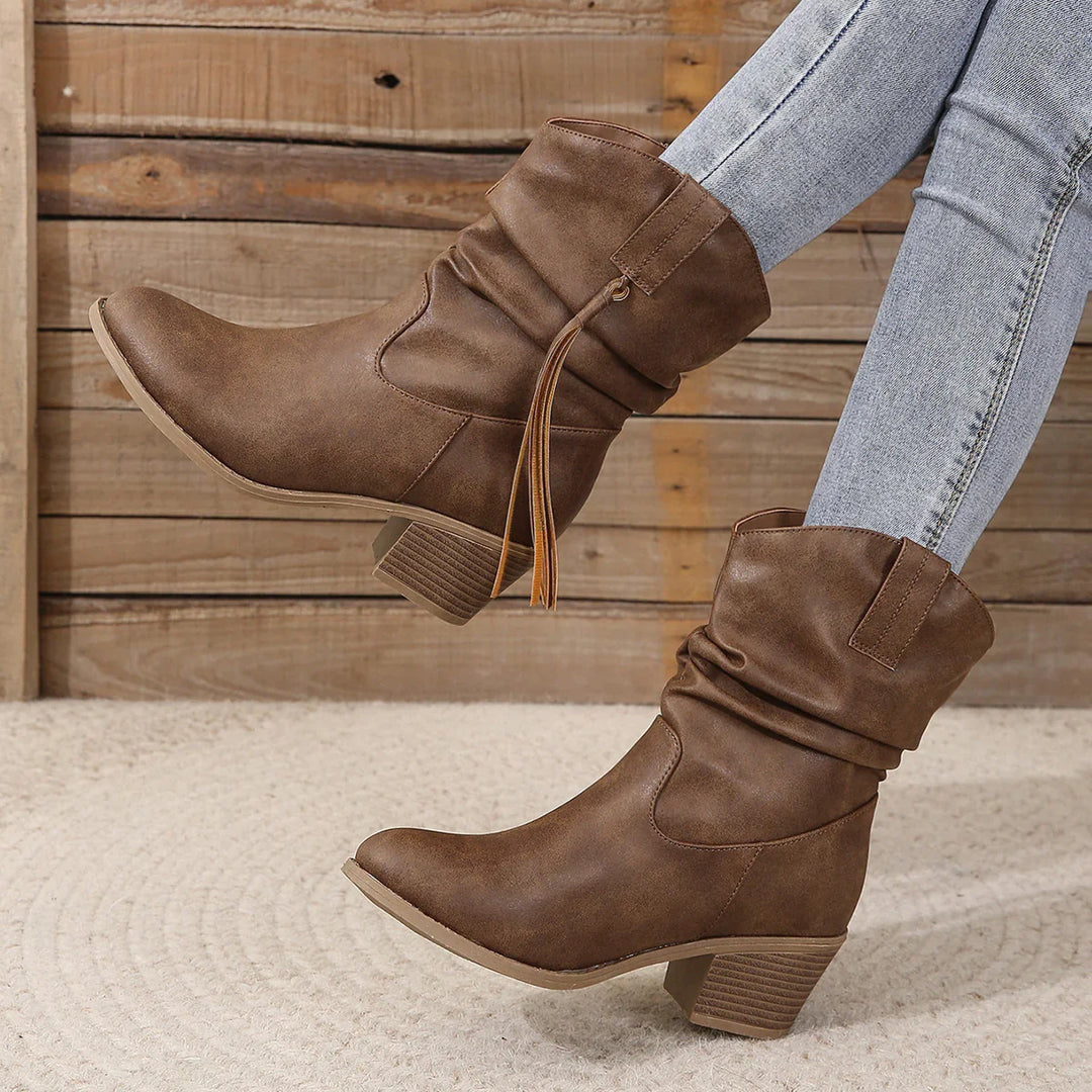 Brown mid-calf slouchy boots with tassel detail worn with light wash skinny jeans on textured carpet