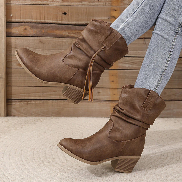 Brown mid-calf slouchy boots with tassel detail worn with light wash skinny jeans on textured carpet