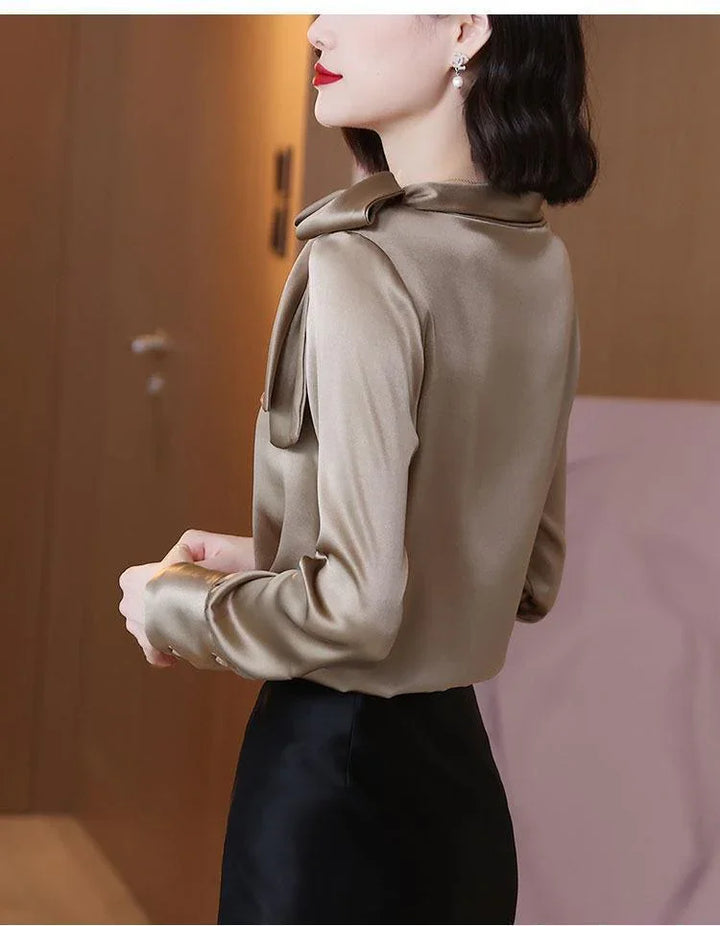 Woman wearing gold satin blouse with bow detail and black skirt in indoor setting