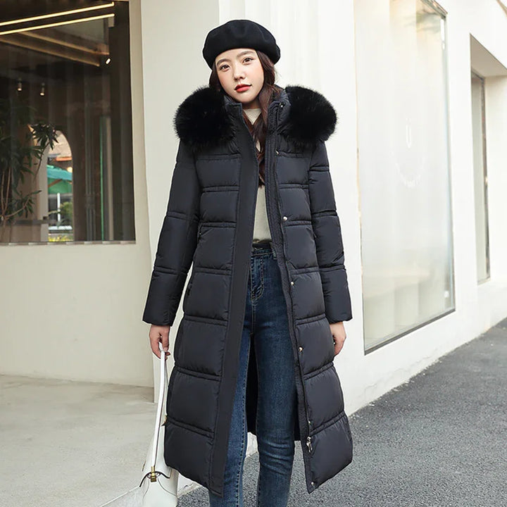 Woman wearing long black puffer coat with fur collar and black beret, holding white handbag outdoors