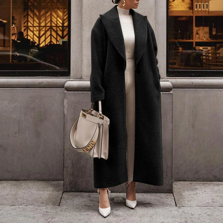 Woman wearing long black coat, white dress, white heels, carrying beige Fendi handbag outdoors