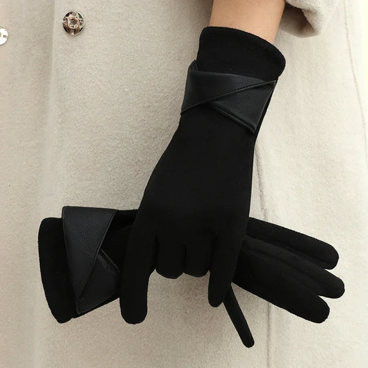 Pair of black winter gloves with leather trim held against beige coat background