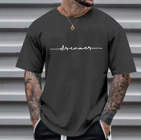 Man wearing black short-sleeve t-shirt with white cursive 'dreamer' text and tattoos on arms