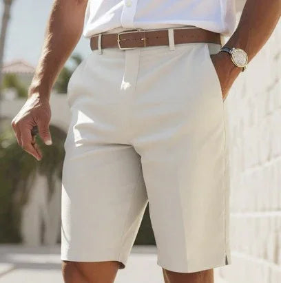 man wearing beige tailored shorts with a brown leather belt and white shirt outdoors
