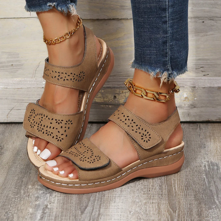 Women's brown open-toe sandals with perforated strap design, worn with frayed denim jeans and gold anklets