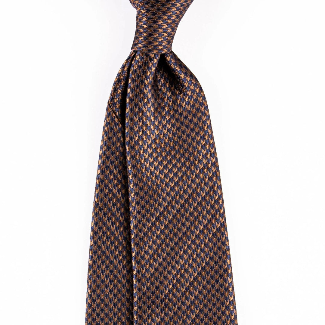 Close-up of blue and bronze patterned silk necktie with a neat knot on white background