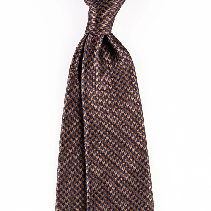 Close-up of blue and bronze patterned silk necktie with a neat knot on white background