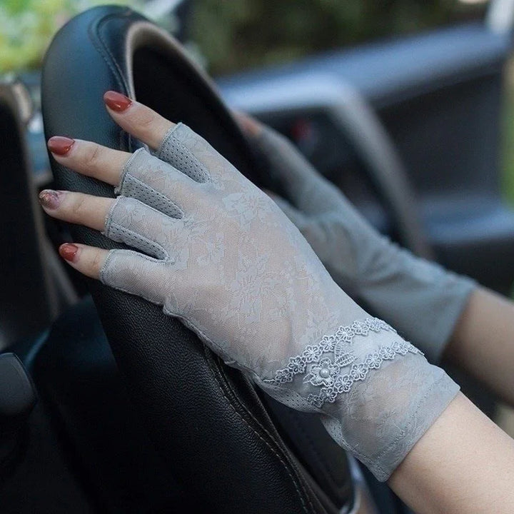 hands wearing elegant gray floral lace fingerless gloves on a black car steering wheel