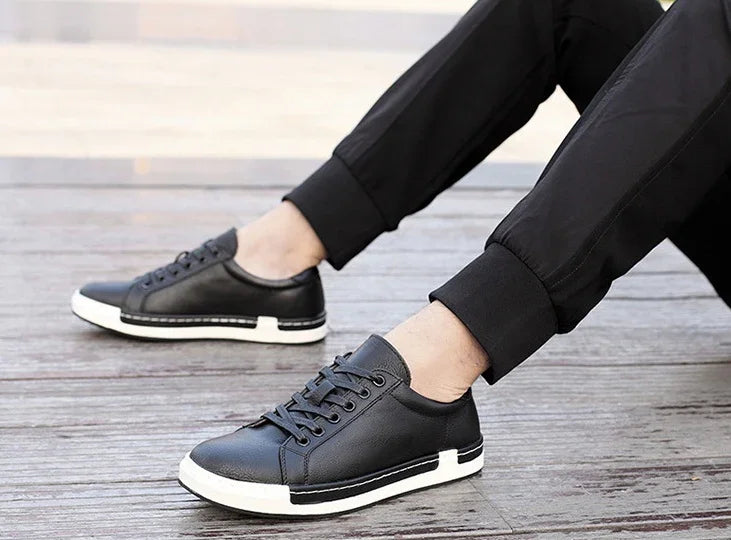 Black leather low-top sneakers with white soles worn with black cuffed pants on wooden floor