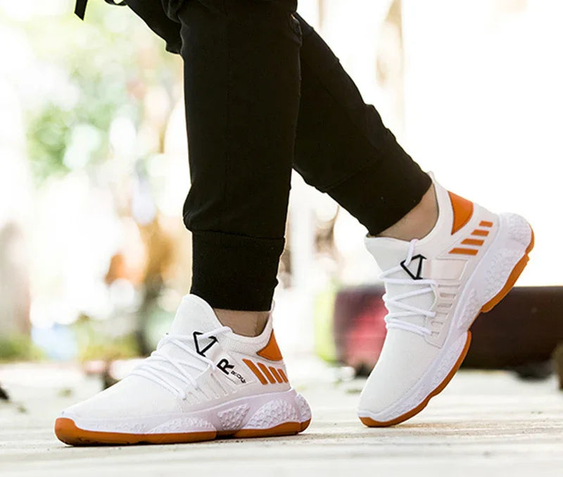 White and orange athletic sneakers with textured soles worn with black joggers on outdoor pavement