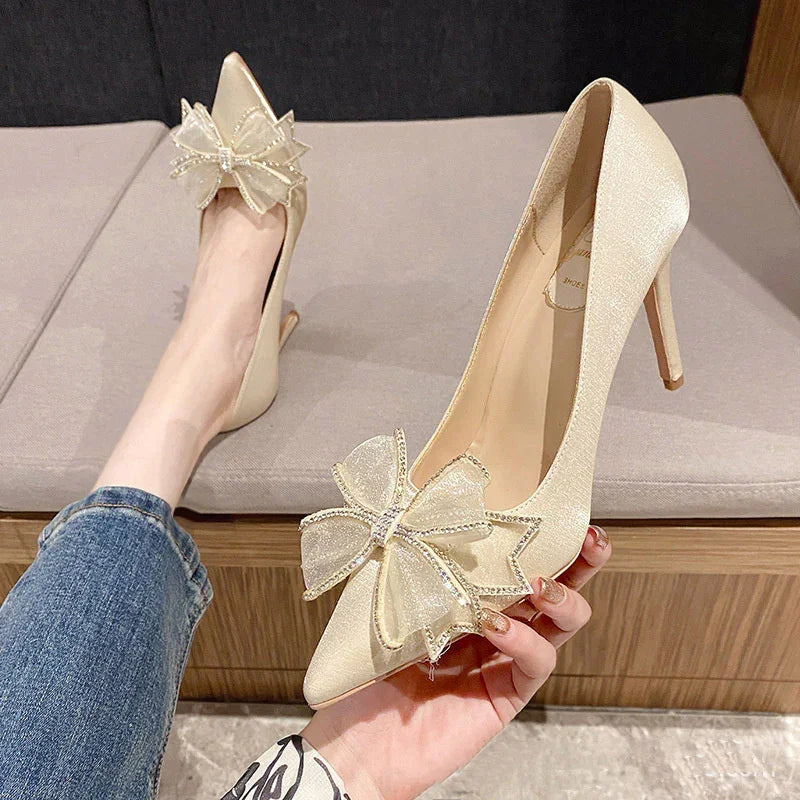 Elegant beige satin high heels with large decorative bows and rhinestone accents