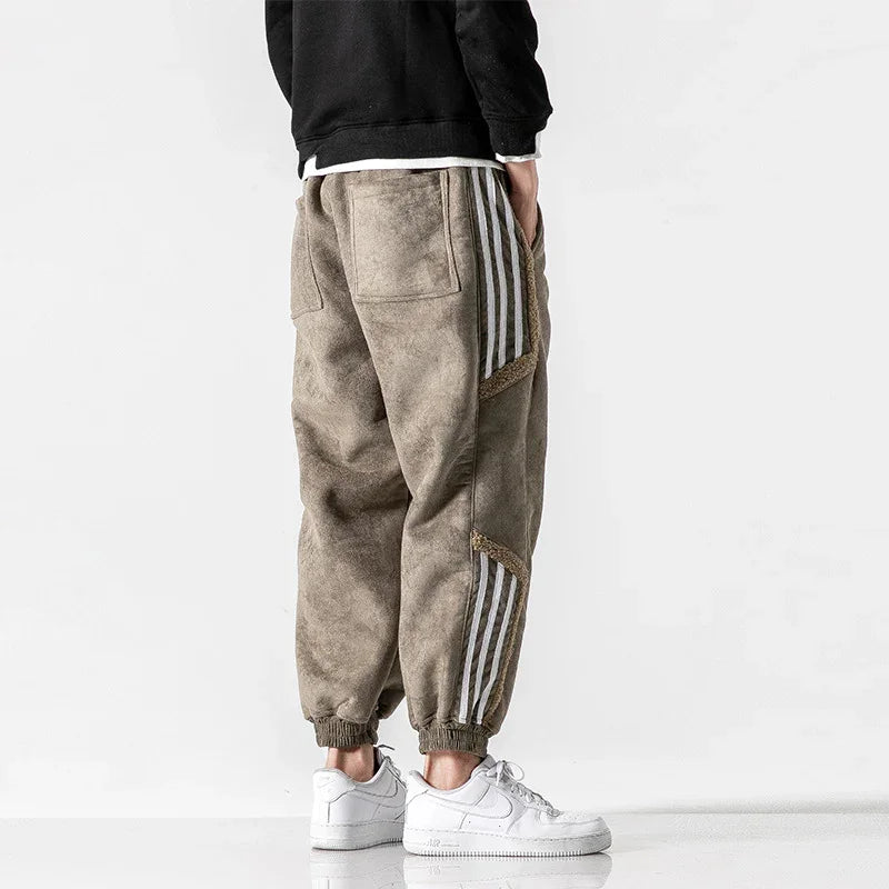 Man wearing brown fleece jogger pants with white stripes and white sneakers on white background