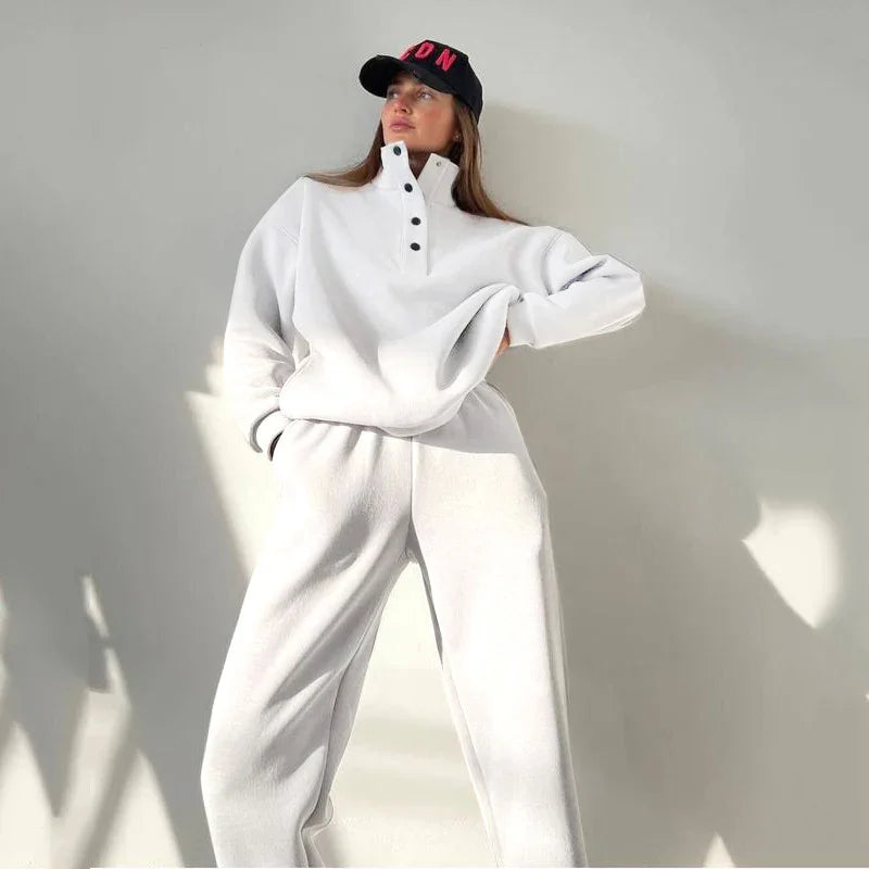 Woman wearing white cozy loungewear set with black snap button collar and black cap with red letters