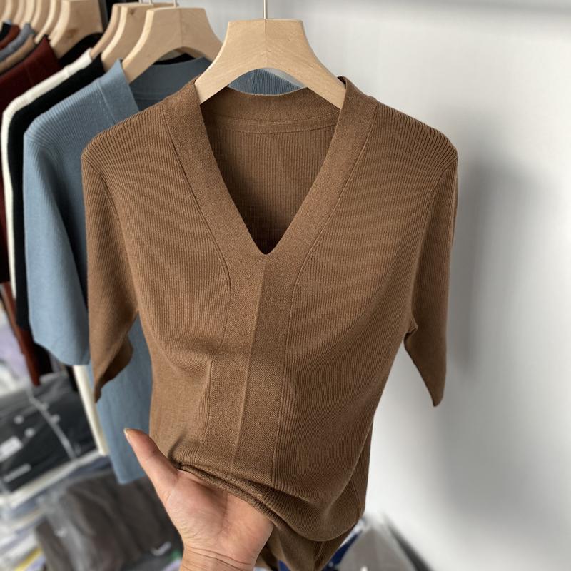 Close-up of a brown ribbed knit V-neck short sleeve sweater held on a wooden hanger with other sweaters in background
