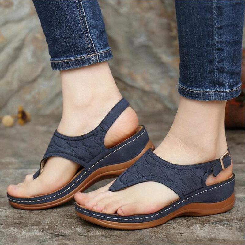 Close-up of feet wearing navy blue wedge sandals with adjustable straps and brown soles on stone surface
