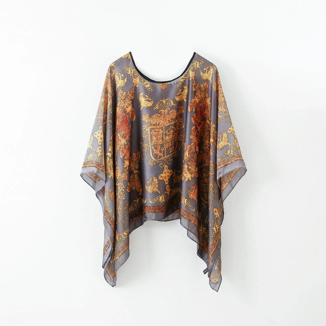 Ornate gray silk poncho with gold and rust baroque pattern hanging on white wall