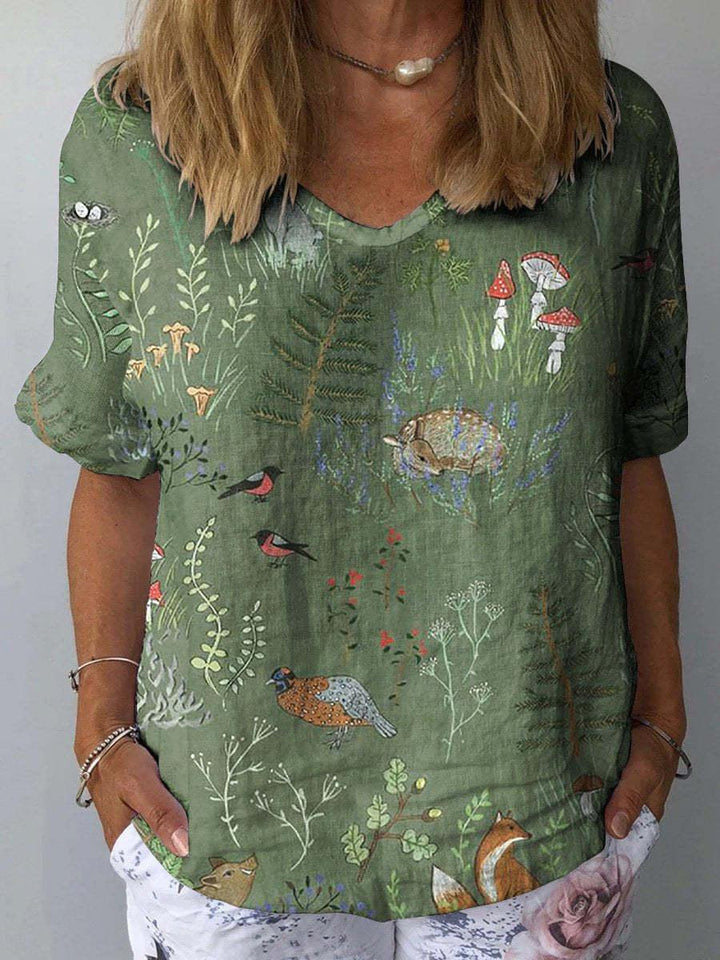 Woman wearing green forest-themed blouse with birds, fox, mushrooms, and plants print