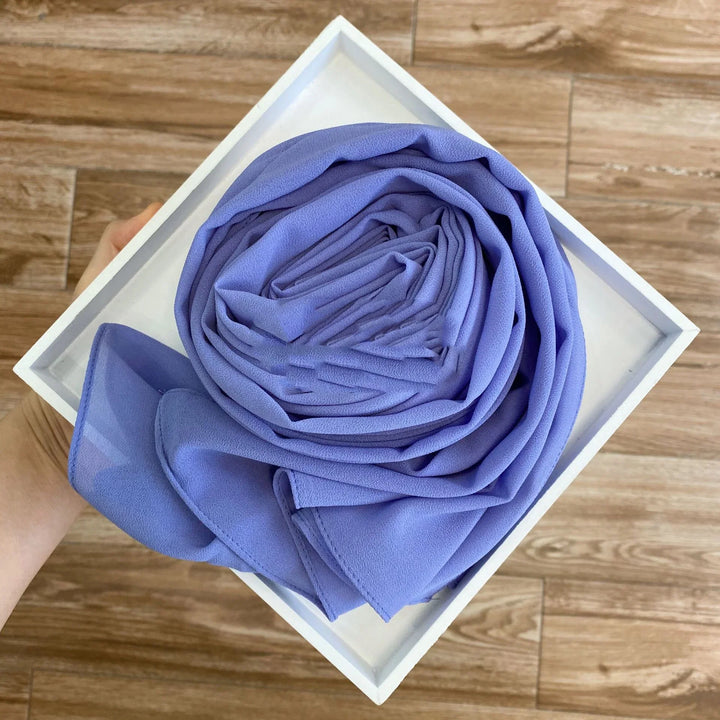 Hand holding a white square tray with a neatly rolled lavender chiffon fabric on wooden floor