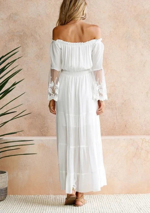 Woman wearing white off-shoulder maxi dress with sheer lace bell sleeves standing indoors