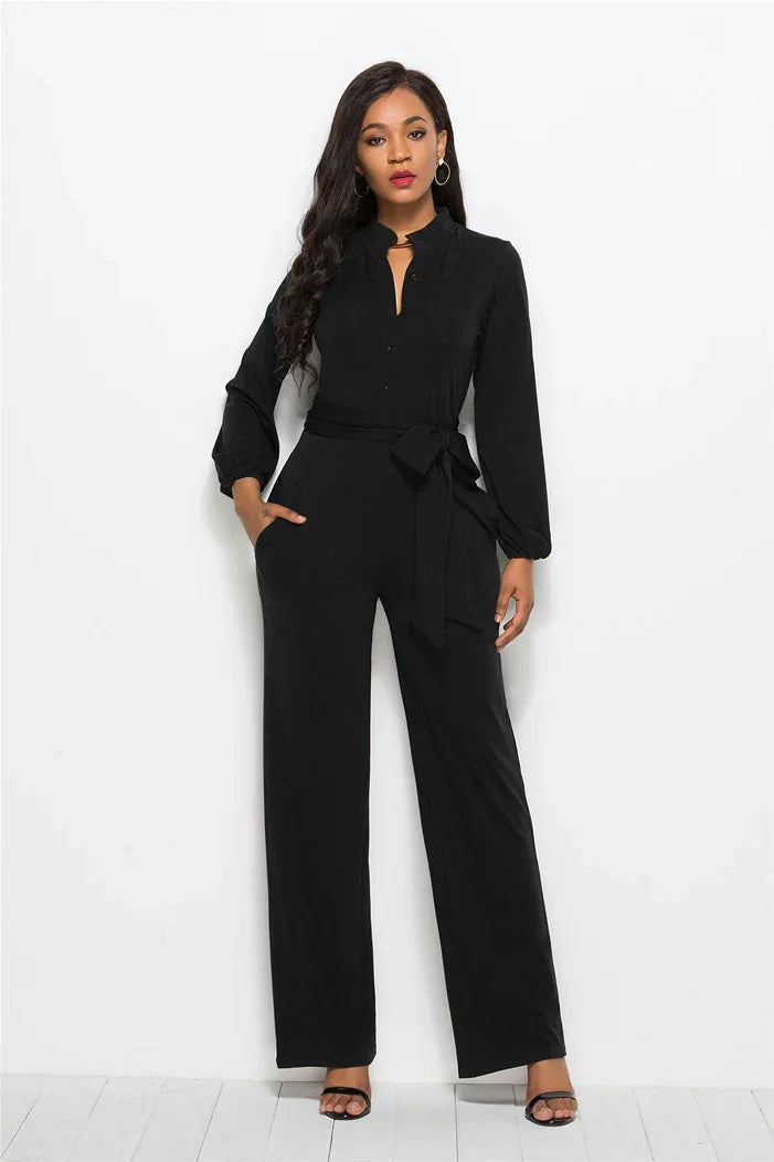 Woman in black long-sleeve jumpsuit with waist tie and wide-leg pants posing against white background