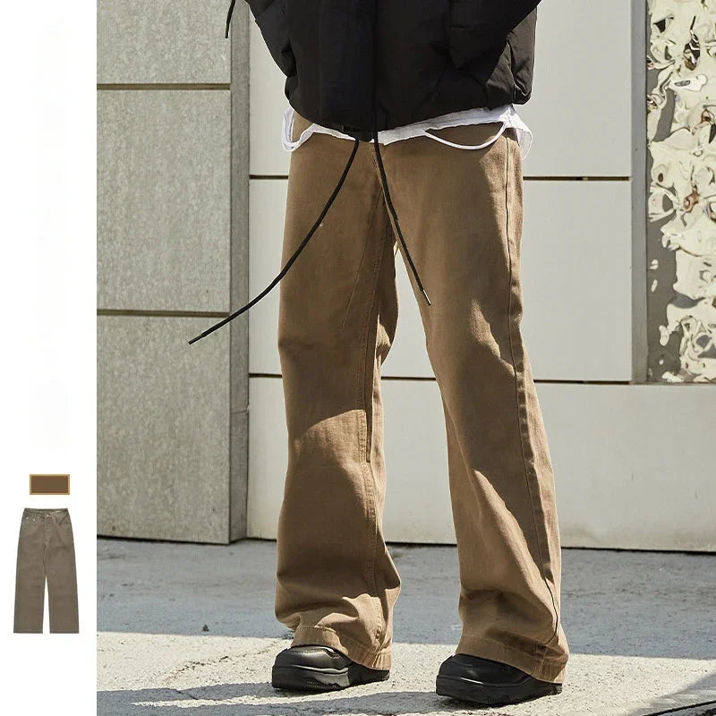 Person wearing loose brown casual pants and black shoes standing outdoors on concrete pavement