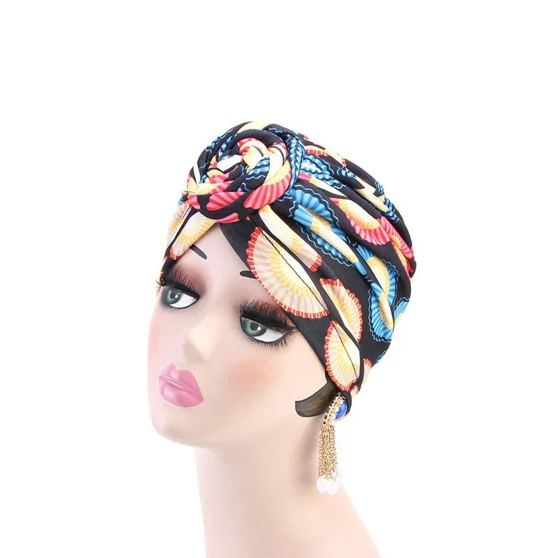 Mannequin head wearing a colorful patterned turban with oversized eyelashes and dangling pearl earrings