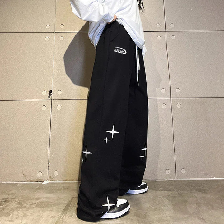 Person wearing black wide-leg sweatpants with white star designs and white drawstrings, paired with black and white sneakers