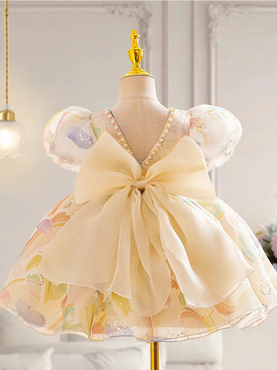 Back view of a pastel floral kids party dress with puff sleeves, pearl neckline, and large cream bow