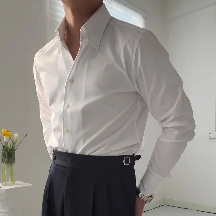 man wearing fitted white dress shirt and high-waist black trousers in minimal indoor setting with flowers
