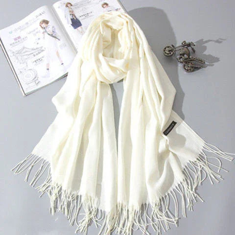 Soft white fringed scarf displayed on gray surface with fashion magazine and vintage key decoration