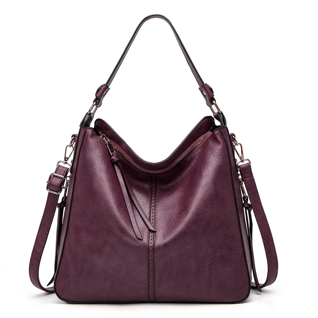 Stylish dark purple leather handbag with gold hardware and adjustable straps on white background