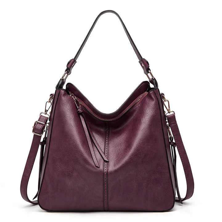 Stylish dark purple leather handbag with gold hardware and adjustable straps on white background