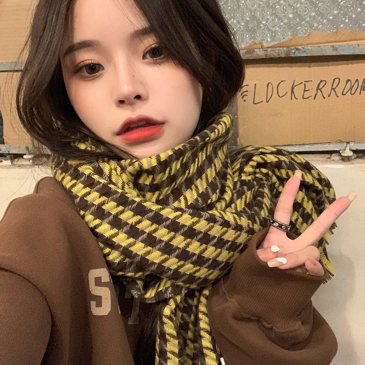 Young woman wearing a brown sweater and yellow-brown checkered scarf making a peace sign indoors