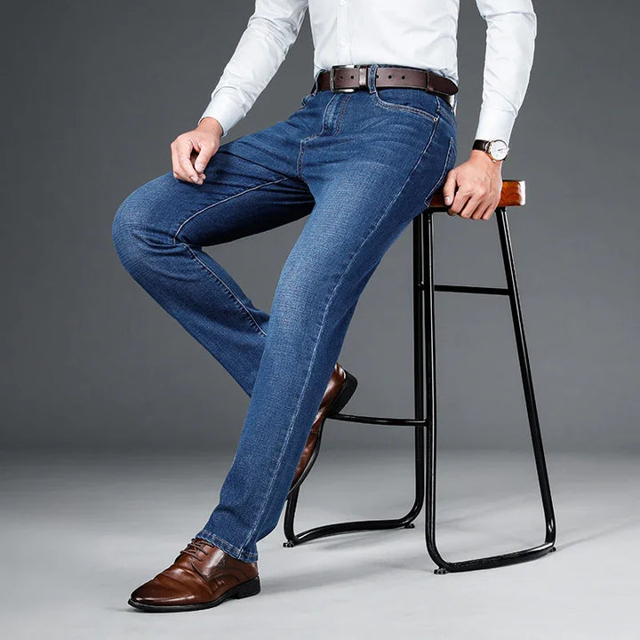 Man wearing blue jeans, white shirt, brown leather belt and shoes sitting on black metal stool