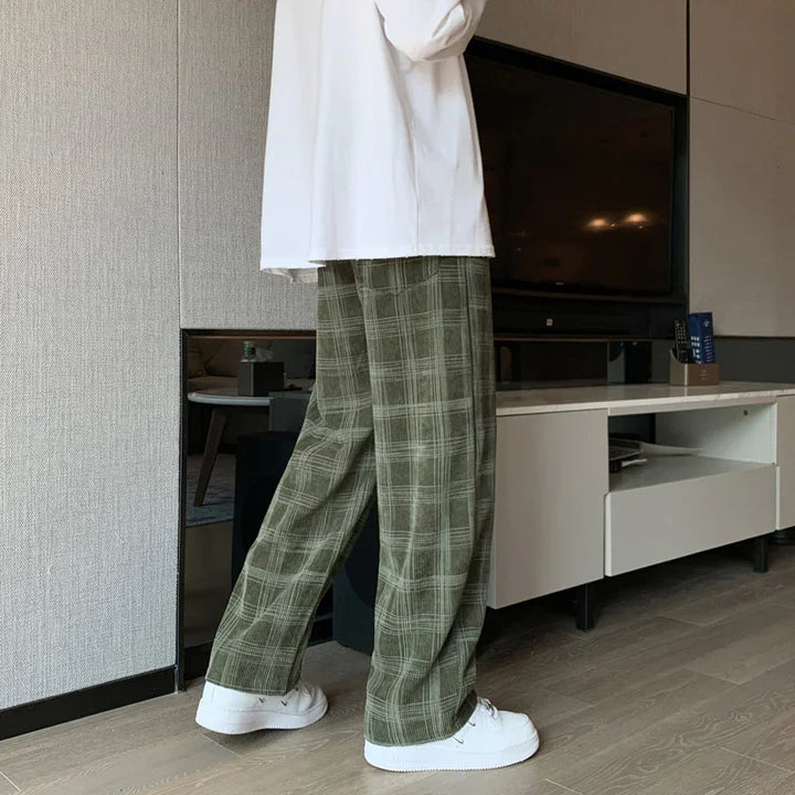 Person wearing green plaid wide-leg pants and white sneakers standing indoors on wooden floor