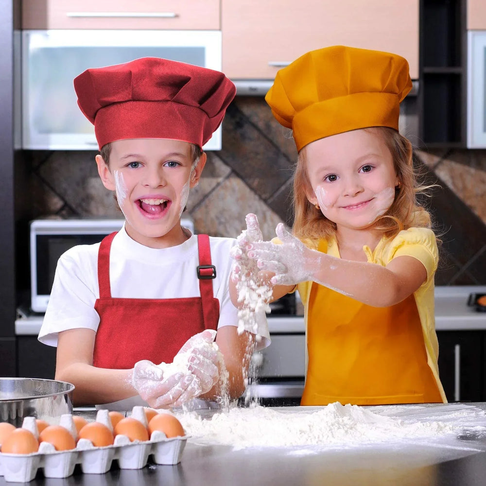 Two children in red and yellow chef hats and aprons playing with flour in a kitchen