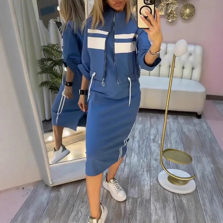 Woman wearing blue sporty two-piece set with white stripes and white sneakers taking mirror selfie indoors