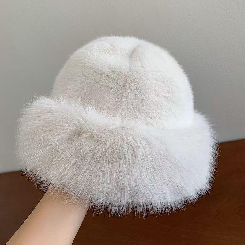 Hand holding a soft white faux fur winter hat with a fluffy brim against gray and brown background