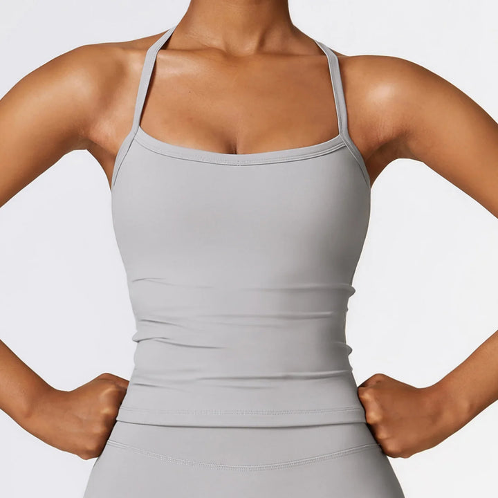Woman wearing light gray fitted workout tank top with thin straps, hands on hips