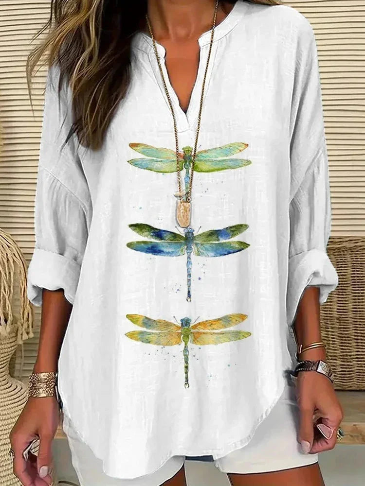 Woman wearing white long-sleeve shirt with colorful dragonfly prints, accessorized with gold bracelets and necklace