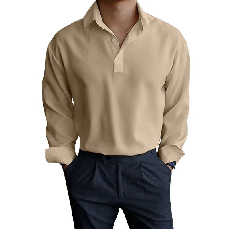 Man wearing beige long sleeve collared shirt with navy blue pleated pants, hands in pockets